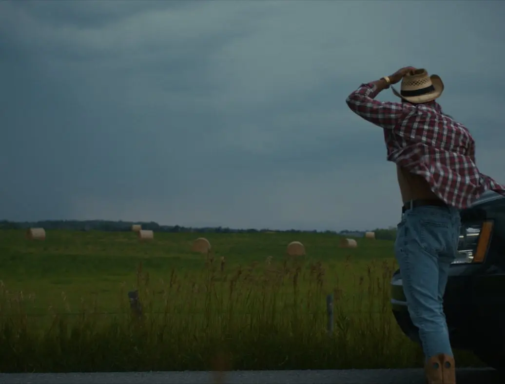 A lone rancher stands in a windstorm.